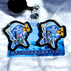 May include: Two blue and black badge reels with cartoon characters holding bones and radiation symbols. The text "RADMARKERS.COM" is printed on the blue background. The badge reels have a black retractable cord and a metal clip.