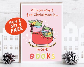 May include: A pink Christmas card featuring a red sleigh laden with books, fairy lights, and holly. The text reads "All you want for Christmas is... more BOOKS." A red circle says "BUY 2 GET 1 FREE."