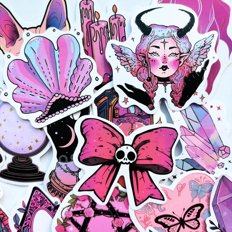 May include: A collection of stickers featuring a variety of designs in shades of pink, purple, and black. The stickers include a seashell, candles, a horned woman with wings, a bow with a skull, crystals, and a butterfly.