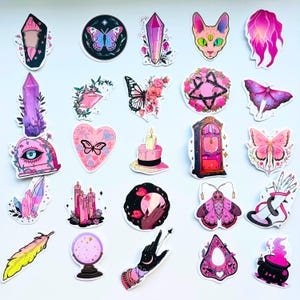 May include: A collection of colorful stickers featuring mystical and witchy designs. The stickers include butterflies, crystals, a cat, a clock, a feather, a fortune-telling ball, and a cauldron. The color palette includes pink, purple, black, and yellow.