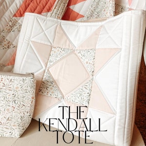 Peut inclure: Un sac cabas blanc avec un motif d'étoile rose et blanche. Le sac a une impression florale sur les poignées et est fait de tissu matelassé. Le texte "THE KENDALL TOTE BY SHELBY MCCOLLUM" est imprimé sur le devant du sac.