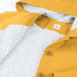 May include: A yellow raincoat with a white lining featuring a blue polka dot pattern. The raincoat has a hood and a button closure.