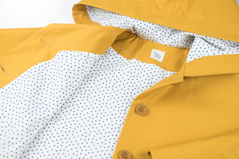May include: A yellow raincoat with a white lining featuring a blue polka dot pattern. The raincoat has a hood and a button closure.