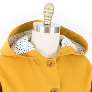 May include: A yellow hooded jacket with a white and blue polka dot lining. The jacket has a button closure.