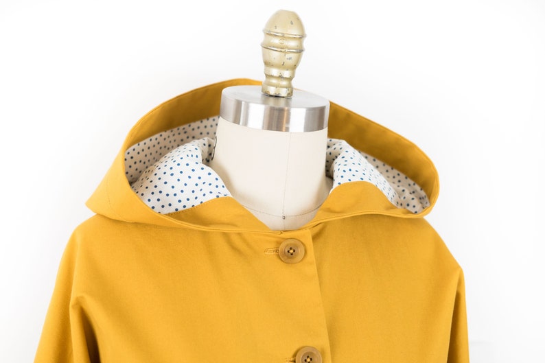 May include: A yellow hooded jacket with a white and blue polka dot lining. The jacket has a button closure.