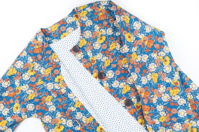 May include: A blue floral fabric with a white polka dot lining. The fabric features a variety of flowers in shades of yellow, orange, and white.