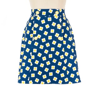 May include: A blue skirt with a white and yellow daisy print. The skirt has a button closure and pockets.