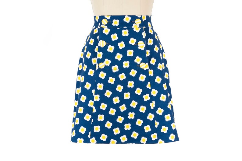 May include: A blue skirt with a white and yellow daisy print. The skirt has a button closure and pockets.