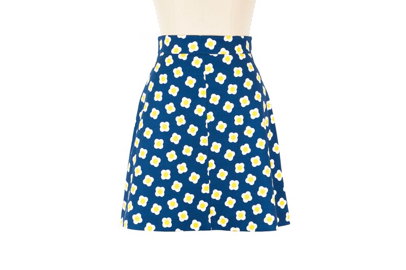 May include: A blue skirt with a white and yellow daisy print.
