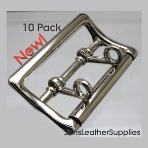 May include: A pack of 10 silver-toned metal belt buckles. The buckles are rectangular with a smooth, polished finish. The text "New!" and "10 Pack" are visible in the image.