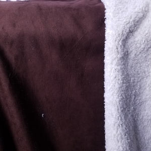 May include: A dark brown blanket with a soft, velvety texture. The blanket is paired with a white, fluffy, sherpa-like material on the right side. The contrasting textures and colours create a cosy aesthetic.