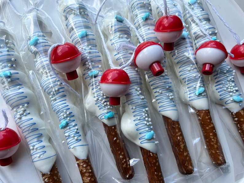 May include: Pretzel rods dipped in white chocolate, decorated with blue drizzle, sugar pearls, and blue fish-shaped sprinkles. Each pretzel is topped with a red and white bobber and packaged in clear cellophane.