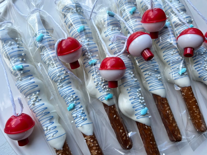 May include: Pretzel rods dipped in white chocolate, decorated with blue lines, fish-shaped sprinkles, and white nonpareils. Each pretzel is packaged and topped with a red and white bobber. A fun, themed treat.