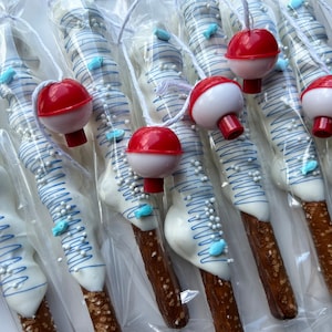 May include: Pretzel rods dipped in white chocolate, decorated with blue lines, sprinkles, and fish-shaped candies. Each pretzel is packaged and topped with a red and white bobber, creating a fishing-themed treat.