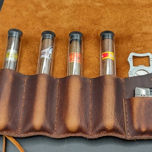 May include: A brown leather cigar case with five slots for cigars, a bottle opener, and a small pocket for a lighter. The case is closed and has a brown leather strap.
