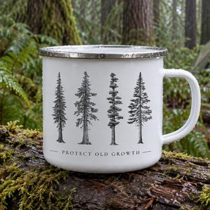 May include: A white enamel mug with a silver rim and a handle, featuring a black graphic illustration of four distinct evergreen trees and the text "PROTECT OLD GROWTH" printed in black lettering centered below the tree designs.