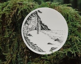 May include: A white ceramic plate featuring a black and white illustration of a coastal landscape with trees, water, and rocks. The plate is round and sits on a moss-covered surface, creating a natural aesthetic.