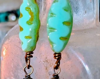 May include: A pair of handcrafted earrings featuring turquoise and green beads. The earrings have a vintage aesthetic with copper-colored wire and decorative teardrop-shaped pendants. The beads have a unique, textured design.