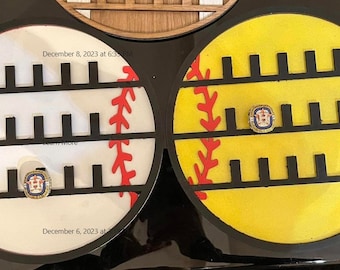 May include: Two round wooden softball display shelves with black trim. Each shelf has three rows of slots for rings or other small items. The shelves are painted to look like a baseball and a softball. The baseball is white with red stitching and the softball is yellow with red stitching. The date December 6, 2023 is written on the bottom of each shelf.
