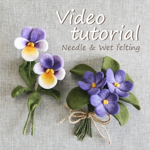 以下が含まれることがあります： 紫、白、黄色、緑色の手作りのフェルトフラワー。画像には2つのアレンジメントが表示されています。個々のパンジーと紐で結ばれた花束です。テキストオーバーレイは「Video tutorial Needle & Wet felting」と表示されています。
