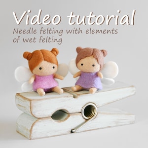 May include: Two felted fairy dolls with orange and brown hair, wearing pink and purple dresses, and white wings, sit on a large, distressed white wooden clothespin. The image includes the text "Video tutorial" and "Needle felting with elements of wet felting."