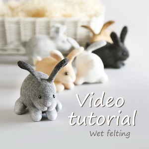 May include: A selection of felted rabbit figures in shades of grey, beige, white, and black. The rabbits are displayed together, with one in the front. The image features the text "Video tutorial" and "Wet felting".