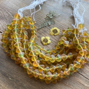 May include: A strand of amber glass beads with a green swirl pattern. The beads are strung on white thread and are arranged in a circular shape.