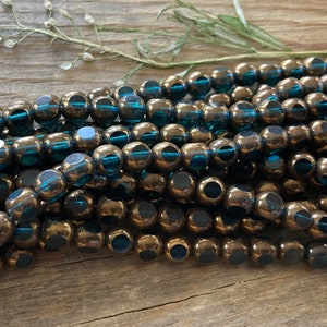 May include: A strand of teal blue glass beads with a bronze metallic finish. The beads have a faceted design and a hole in the center.