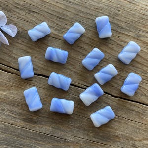 May include: A collection of 14 light blue glass tiles with a white swirl pattern. The tiles are arranged on a wooden surface.