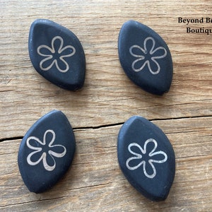 May include: Four black ceramic leaf-shaped beads with a white stylized flower design. Beyond Beads Boutique.