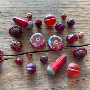 May include: Assortment of red glass beads, including round, faceted, and teardrop shapes. Some beads have a floral design.