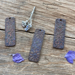 May include: Three rectangular metal charms with a floral design. The charms are a dark brown color with a hint of purple.