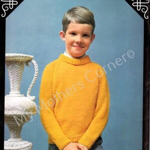 May include: A young boy wearing a yellow knitted sweater with a crew neck. He is standing in front of a white vase.