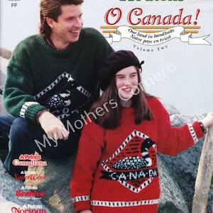 May include: A red and white knitted sweater with a loon and the word "CANADA" in a diamond shape. The sweater is worn by a person with a black beret. The background is a rocky beach.