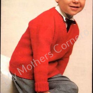 May include: A red knitted sweater with a V-neck and long sleeves. The sweater is worn by a young boy with dark hair and a white shirt underneath.