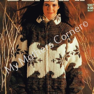 Puede incluir: Una mujer con una chaqueta de punto marrón, crema y negra con un diseño de copos de nieve y olas. La chaqueta tiene cierre de cremallera y cuello alto. La palabra "BERNAT" está en la parte superior de la imagen y "NORTHERN Spirit" en la inferior.