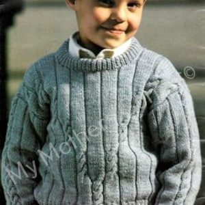 Può includere: Un maglione di lana blu chiaro con un motivo a treccia. Il maglione ha un collo rotondo e maniche lunghe.