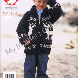 Peut inclure: Un pull en tricot noir et blanc avec une fermeture éclair et un motif de renne. Le pull est porté par un jeune garçon portant un chapeau et un jean bleu. Le texte "White Buffalo 102" et "Made in Canada... where we know cold." est imprimé sur l'image.