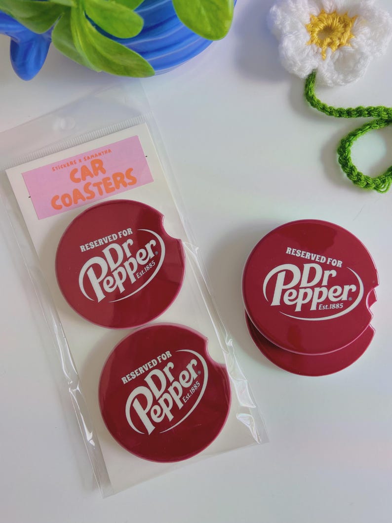 May include: Three red car coasters featuring the Dr Pepper logo in white. The coasters are circular with a convenient notch. The packaging includes a pink label that reads "STICKERS & SAMASTRA CAR COASTERS".