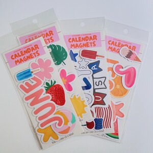 May include: Three clear plastic packages of calendar magnets labeled CALENDAR MAGNETS. The stickers feature colorful summer-themed designs including a strawberry, a beach ball, a popsicle, a flamingo, an orange slice, and the text JUNE.