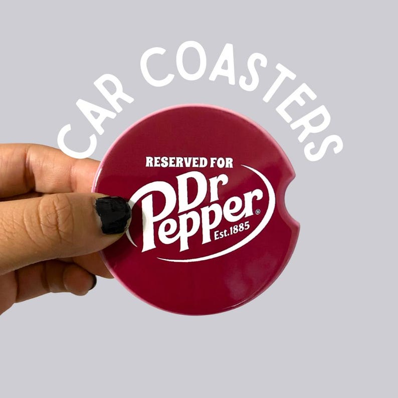May include: A burgundy car coaster featuring the Dr. Pepper logo in white. The coaster has a curved cutout for easy removal and the text "RESERVED FOR Dr Pepper Est.1885". The words "CAR COASTERS" are arched above the coaster.