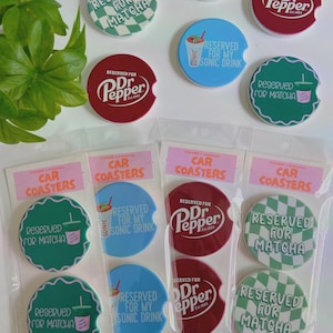 May include: A collection of car coasters featuring text like "Reserved for Matcha" and "Reserved for Dr. Pepper." The coasters are circular, with some having a scalloped edge. They are available in green, red, and blue, and are packaged.