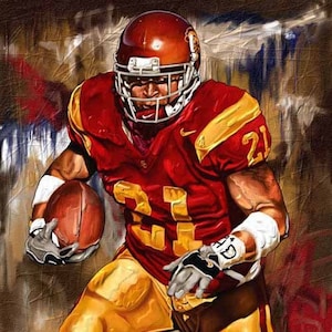 May include: A football player wearing a red and gold uniform with the number 21 on the jersey. He is holding a football and wearing a helmet with a face mask. The background is a blurred image of a football field.