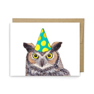 May include: A greeting card featuring a watercolor illustration of a grey and brown owl with bright yellow eyes wearing a teal party hat with yellow polka dots, positioned in front of a plain brown envelope.