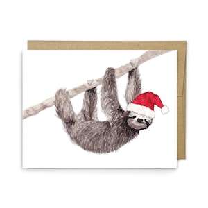 May include: A watercolor illustration on a white greeting card featuring a brown sloth hanging from a light brown tree branch. The sloth is wearing a bright red Santa hat with a white pom-pom and a white trim, set against a plain envelope.