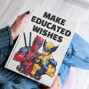 Puede incluir: Una libreta blanca con el texto "MAKE EDUCATED WISHES" en negro. La libreta presenta una imagen de dibujos animados de Deadpool y Wolverine.