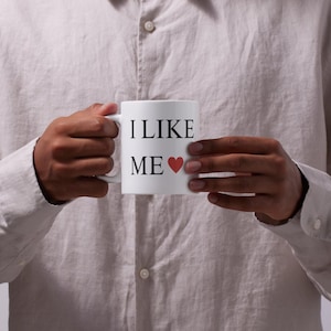 May include: White ceramic mug with black text that reads "I LIKE ME" and a red heart.