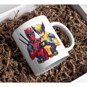 May include: White ceramic mug with a graphic of Deadpool and Wolverine, both characters are depicted with their signature poses and colors. The mug has a black handle.
