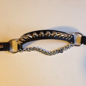 Puede incluir: Un collar de cuero negro con tachuelas piramidales plateadas y una cadena plateada unida.