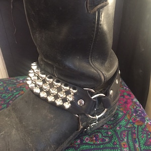 May include: Black leather motorcycle boots with a silver studded strap around the ankle.